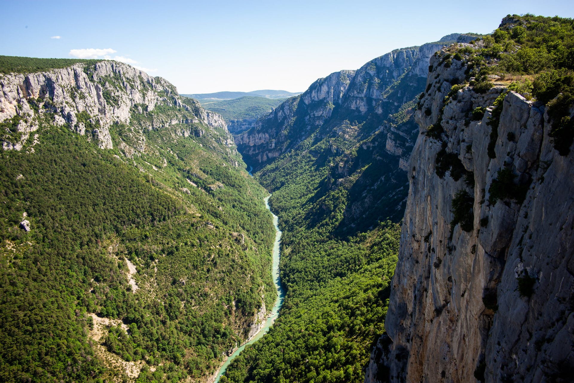Eine tiefe Flussschlucht mit steilen Felsklippen und dichtem grünen Wald, der den Talboden bedeckt, unter einem klaren blauen Himmel.