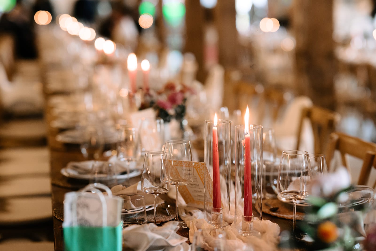 Ein langer, für eine Veranstaltung gedeckter Tisch mit Weingläsern, Tellern, rosafarbenen Kerzen und floralen Tafelaufsätzen, arrangiert in einem sanft beleuchteten Innenraum.